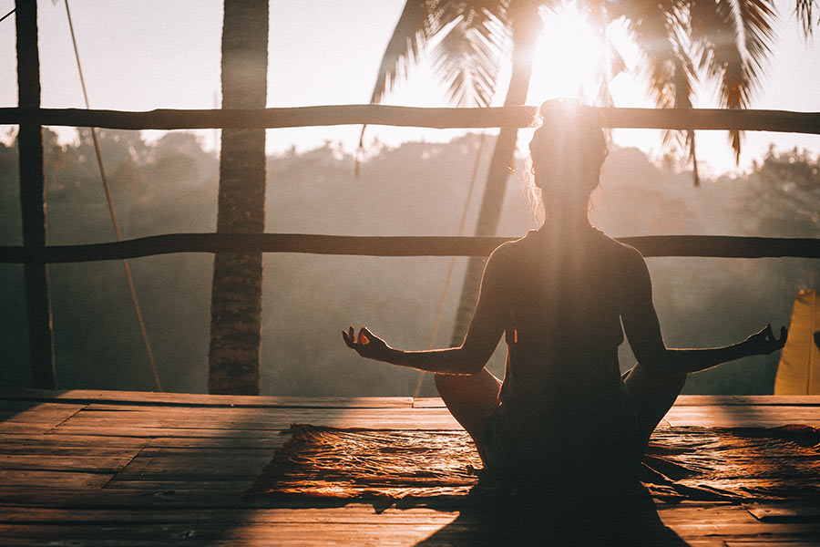 woman sitting in yoga pose silhouetted against the sun in a tropical location